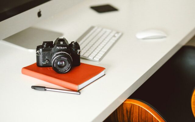 Cámara de fotos y cuaderno sobre una mesa blanca, preparados para escribir