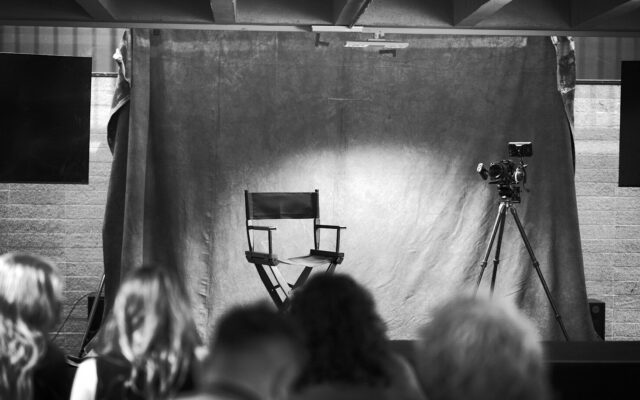 Rodaje en blanco y negro de un biopic, con la silla del director y el público mirando la escena
